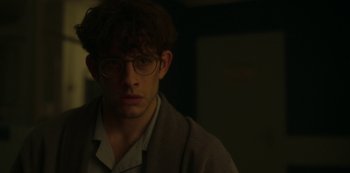 Movie still from “The Girl in the Mirror” (2022), created by Sergio G. Sánchez – A young man wearing glasses looking at the camera; Close Up shot, Over the shoulder angle