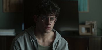 Movie still from “The Girl in the Mirror” (2022), created by Sergio G. Sánchez – A young man wearing glasses and a hooded sweatshirt; Close Up shot, Over the shoulder angle