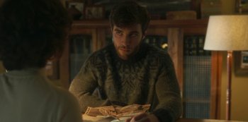 Movie still from “The Girl in the Mirror” (2022), created by Sergio G. Sánchez – A man sitting at a table with a book in his hands; Close Up shot, Over the shoulder angle