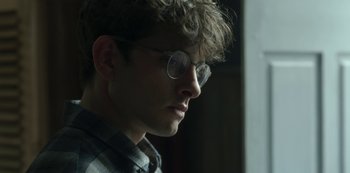 Movie still from “The Girl in the Mirror” (2022), created by Sergio G. Sánchez – A young man wearing glasses looking to his left; Close Up shot, Over the shoulder angle