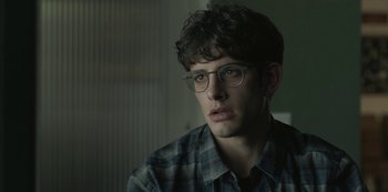Movie still from “The Girl in the Mirror” (2022), created by Sergio G. Sánchez – A young man wearing glasses and a checkered shirt; Close Up shot, Over the shoulder angle