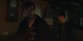 Movie still from “The Girl in the Mirror” (2022), created by Sergio G. Sánchez – A man standing in a room with his hand over his mouth; Medium shot, Over the shoulder angle