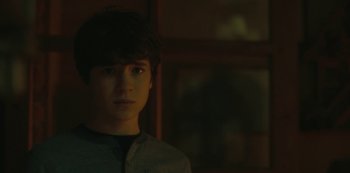 Movie still from “The Girl in the Mirror” (2022), created by Sergio G. Sánchez – A young man is looking at the camera while standing in front of a window; Close Up shot, Over the shoulder angle