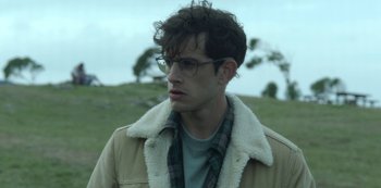 Movie still from “The Girl in the Mirror” (2022), created by Sergio G. Sánchez – A young man wearing glasses and a jacket; Close Up shot, Over the shoulder angle