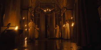 Movie still from “The Girl in the Mirror” (2022), created by Sergio G. Sánchez – A group of people dressed in white are standing in front of a building; Wide shot, Low angle