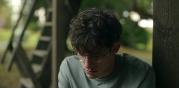Movie still from “The Girl in the Mirror” (2022), created by Sergio G. Sánchez – A young man with glasses is looking down; Close Up shot, Over the shoulder angle