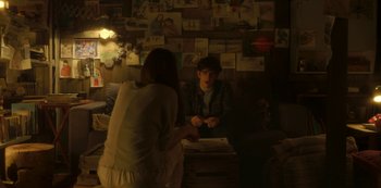 Movie still from “The Girl in the Mirror” (2022), created by Sergio G. Sánchez – A man and a woman sitting at a table in a room; Medium shot, Over the shoulder angle