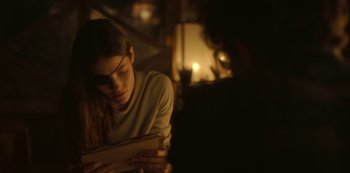 Movie still from “The Girl in the Mirror” (2022), created by Sergio G. Sánchez – A woman sitting in front of a window holding an open book; Close Up shot, Over the shoulder angle