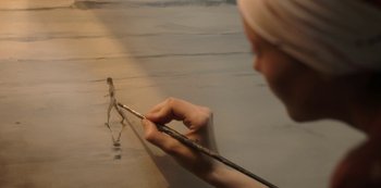 Movie still from “The Girl in the Mirror” (2022), created by Sergio G. Sánchez – A woman holding a pair of chopsticks while painting a picture; Extreme Close Up shot, Low angle