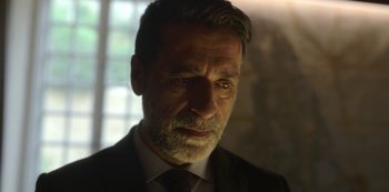 Movie still from “The Girl in the Mirror” (2022), created by Sergio G. Sánchez – A person wearing a suit and tie; Close Up shot, Low angle