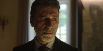 Movie still from “The Girl in the Mirror” (2022), created by Sergio G. Sánchez – A person wearing a suit and tie; Close Up shot, Low angle