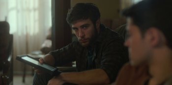 Movie still from “The Girl in the Mirror” (2022), created by Sergio G. Sánchez – A man sitting on top of a couch holding a cell phone; Close Up shot, Over the shoulder angle