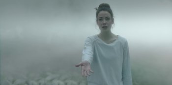 Movie still from “The Girl in the Mirror” (2022), created by Sergio G. Sánchez – A young woman in a white shirt is reaching out her hand to the camera; Close Up shot, Over the shoulder angle