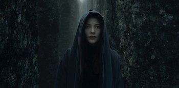 Movie still from “The Girl in the Mirror” (2022), created by Sergio G. Sánchez – A woman in a hooded cloak standing in a forest; Close Up shot, Low angle