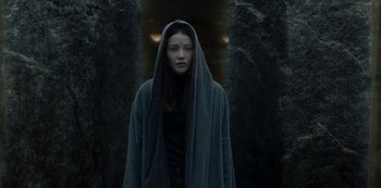 Movie still from “The Girl in the Mirror” (2022), created by Sergio G. Sánchez – A woman standing in front of a stone wall wearing a robe; Medium shot, Low angle