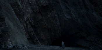 Movie still from “The Girl in the Mirror” (2022), created by Sergio G. Sánchez – A person standing in front of a cave; Extreme Wide shot, Low angle