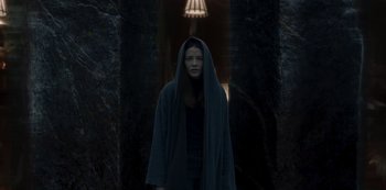 Movie still from “The Girl in the Mirror” (2022), created by Sergio G. Sánchez – A woman in a black robe standing next to a lamp; Medium shot, Low angle