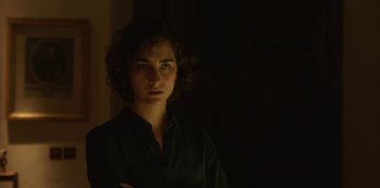 Movie still from “The Girl in the Mirror” (2022), created by Sergio G. Sánchez – A woman standing in a dark room with her arms crossed; Close Up shot, Low angle