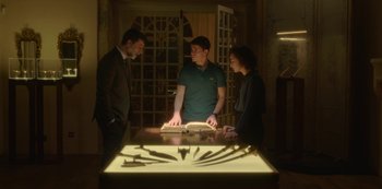 Movie still from “The Girl in the Mirror” (2022), created by Sergio G. Sánchez – Three people standing in front of a table with knives on it; Medium shot, Low angle