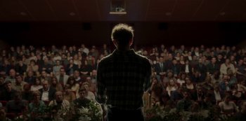 Movie still from “The Girl in the Mirror” (2022), created by Sergio G. Sánchez – A man standing in front of a crowd of people; Wide shot, Low angle