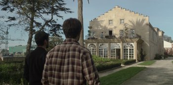 Movie still from “The Girl in the Mirror” (2022), created by Sergio G. Sánchez – Two men standing in front of an old building; Extreme Wide shot, Low angle