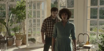 Movie still from “The Girl in the Mirror” (2022), created by Sergio G. Sánchez – A man and a woman standing next to each other in a room; Medium shot, Over the shoulder angle
