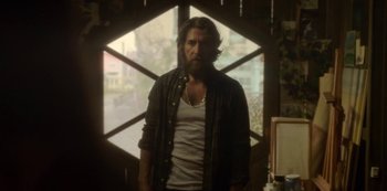 Movie still from “The Girl in the Mirror” (2022), created by Sergio G. Sánchez – A man standing in front of a window with a beard; Medium shot, Over the shoulder angle