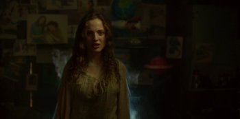 Movie still from “The Girl in the Mirror” (2022), created by Sergio G. Sánchez – A woman standing in front of a wall with pictures on the wall; Medium shot, Low angle