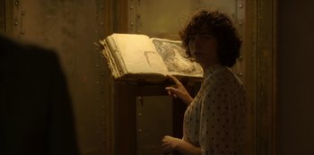Movie still from “The Girl in the Mirror” (2022), created by Sergio G. Sánchez – A woman standing in front of an open book; Medium shot, Over the shoulder angle
