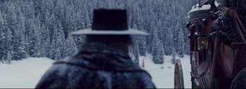Movie still from “The Hateful Eight” (2015), directed by Quentin Tarantino – A man wearing a hat standing in front of a snowy forest; Wide shot, Over the shoulder angle