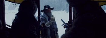 Movie still from “The Hateful Eight” (2015), directed by Quentin Tarantino – A man holding a piece of bread while standing in the snow; Medium shot, Over the shoulder angle