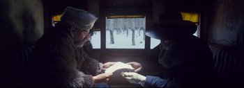 Movie still from “The Hateful Eight” (2015), directed by Quentin Tarantino – Two men are holding a piece of paper in front of a window; Medium shot, Overhead angle