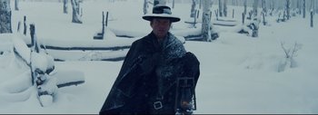 Movie still from “The Hateful Eight” (2015), directed by Quentin Tarantino – A man in a black coat and hat holding a lantern in the snow; Medium shot, Low angle
