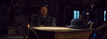 Movie still from “The Hateful Eight” (2015), directed by Quentin Tarantino – A man sitting at a wooden table in a room; Medium shot, Low angle