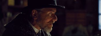 Movie still from “The Hateful Eight” (2015), directed by Quentin Tarantino – An old man with a beard wearing a black hat; Close Up shot, Over the shoulder angle