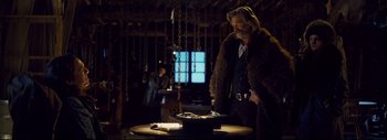Movie still from “The Hateful Eight” (2015), directed by Quentin Tarantino – A man standing in front of a table with chains; Medium shot, Over the shoulder angle