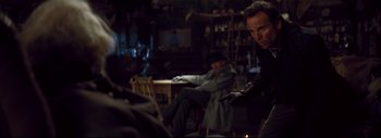 Movie still from “The Hateful Eight” (2015), directed by Quentin Tarantino – Two men sitting at a table in a dark room; Medium shot, Over the shoulder angle