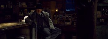 Movie still from “The Hateful Eight” (2015), directed by Quentin Tarantino – A man sitting in a chair wearing a hat and a coat; Medium shot, Low angle