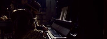 Movie still from “The Hateful Eight” (2015), directed by Quentin Tarantino – A man in a fur coat playing a piano; Medium shot, Low angle