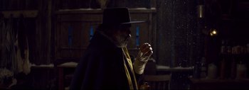 Movie still from “The Hateful Eight” (2015), directed by Quentin Tarantino – An old man wearing a black hat and holding a bottle; Medium shot, Over the shoulder angle