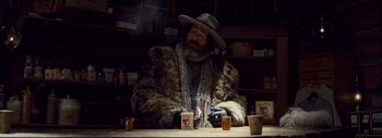 Movie still from “The Hateful Eight” (2015), directed by Quentin Tarantino – A man sitting at a table in a store; Medium shot, Low angle