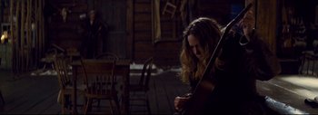 Movie still from “The Hateful Eight” (2015), directed by Quentin Tarantino – A woman is playing a violin in a dark room; Medium shot, High angle