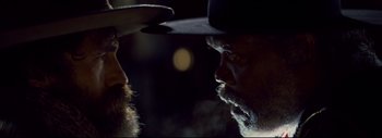 Movie still from “The Hateful Eight” (2015), directed by Quentin Tarantino – A man with a beard wearing a black hat; Close Up shot, Over the shoulder angle