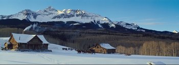 Movie still from “The Hateful Eight” (2015), directed by Quentin Tarantino – A group of horses pulling a wagon down a snow covered road; Extreme Wide shot, High angle
