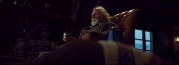 Movie still from “The Hateful Eight” (2015), directed by Quentin Tarantino – An older man sitting on a couch holding a drink; Medium shot, Low angle