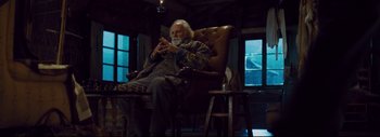 Movie still from “The Hateful Eight” (2015), directed by Quentin Tarantino – An older man sitting in a chair looking at his cell phone; Medium shot, Low angle