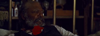 Movie still from “The Hateful Eight” (2015), directed by Quentin Tarantino – An older man smoking a cigarette while wearing a suit; Close Up shot, Over the shoulder angle