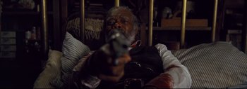 Movie still from “The Hateful Eight” (2015), directed by Quentin Tarantino – An older man holding a gun while sitting in a chair; Close Up shot, Over the shoulder angle