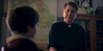 Movie still from “The Haunting of Bly Manor” (2020), directed by E.L. Katz – A man wearing a priest's collar talking to a young boy; Close Up shot, Over the shoulder angle