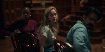 Movie still from “The Haunting of Bly Manor” (2020), directed by E.L. Katz – A woman standing in front of other people in a room; Medium shot, Over the shoulder angle